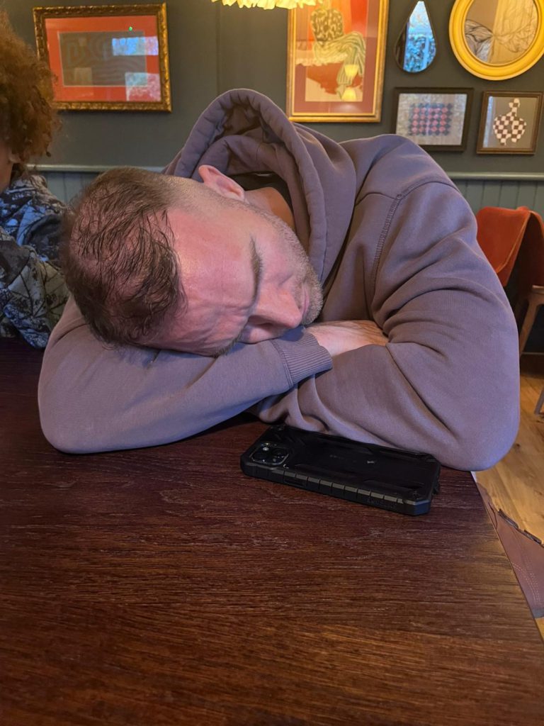 A quiet family moment at home during autumn 2024 — the children playing while John sits apart, visibly weighed down