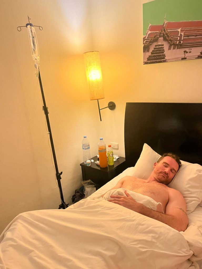 John on a drip in the hotel room in Thailand over Christmas, having become severely dehydrated with sickness — a low point in an already difficult trip
