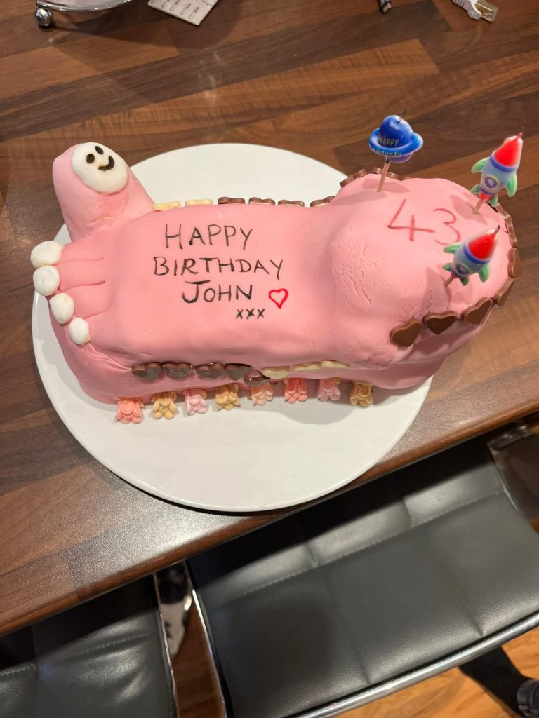 The celebration cake made for John's birthday, featuring a fondant big toe lifting up — a family joke marking what they hoped was the end of the foot problems